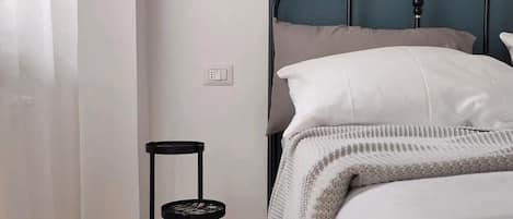 A bedroom with a bed, a chair, a hanging light fixture, and a wall socket.