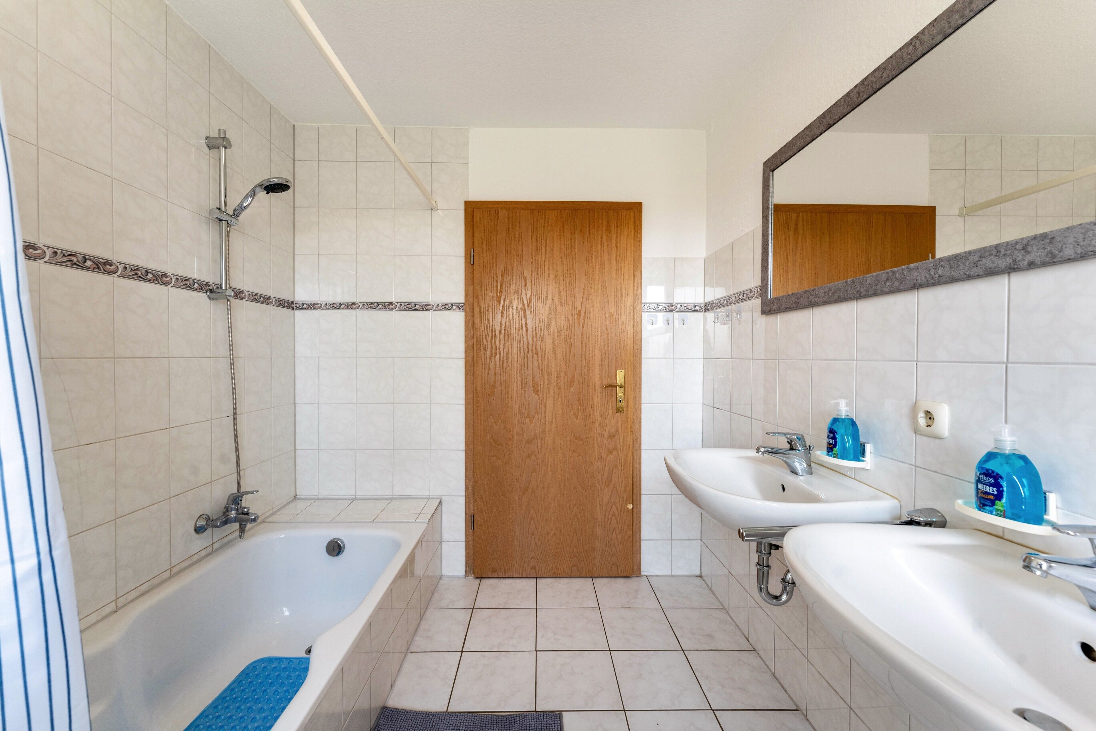 Ein Badezimmer mit Badewanne, zwei Waschbecken, Dusche und Holztür.