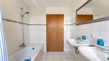 Ein Badezimmer mit Badewanne, zwei Waschbecken, Dusche und Holztür.