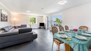 Un salon moderne avec un canapé, une table à manger dressée pour quatre personnes et un téléviseur.