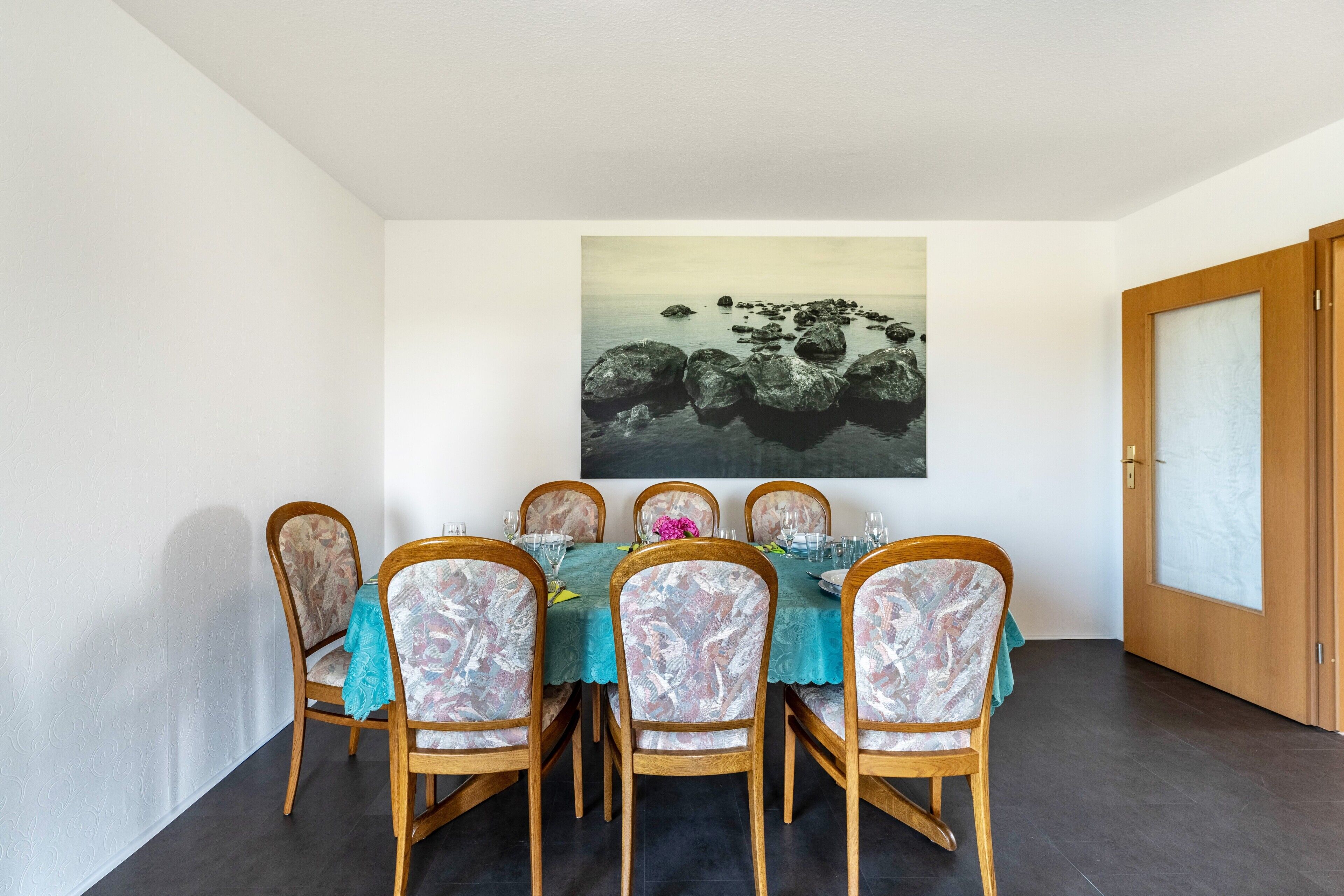 Ein Essbereich mit einem Tisch für sechs Personen, Holzsesseln und einem großen Gemälde an der Wand.