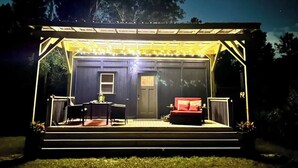 Ein überdachter Außenbereich mit Tisch und Stühlen, einem roten Sofa und einer Tür.