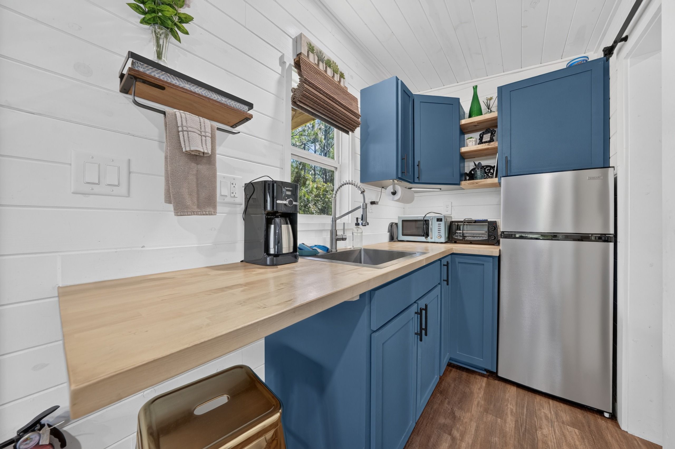 Una cocina moderna con encimera de madera, armarios azules, un refrigerador de acero inoxidable y una cafetera.