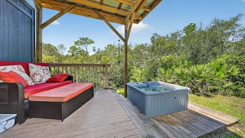 Una terraza de madera con un jacuzzi y un sofá con cojines rojos.