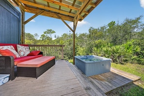 Eine Holzterrasse mit Whirlpool und einer Couch mit roten Kissen.
