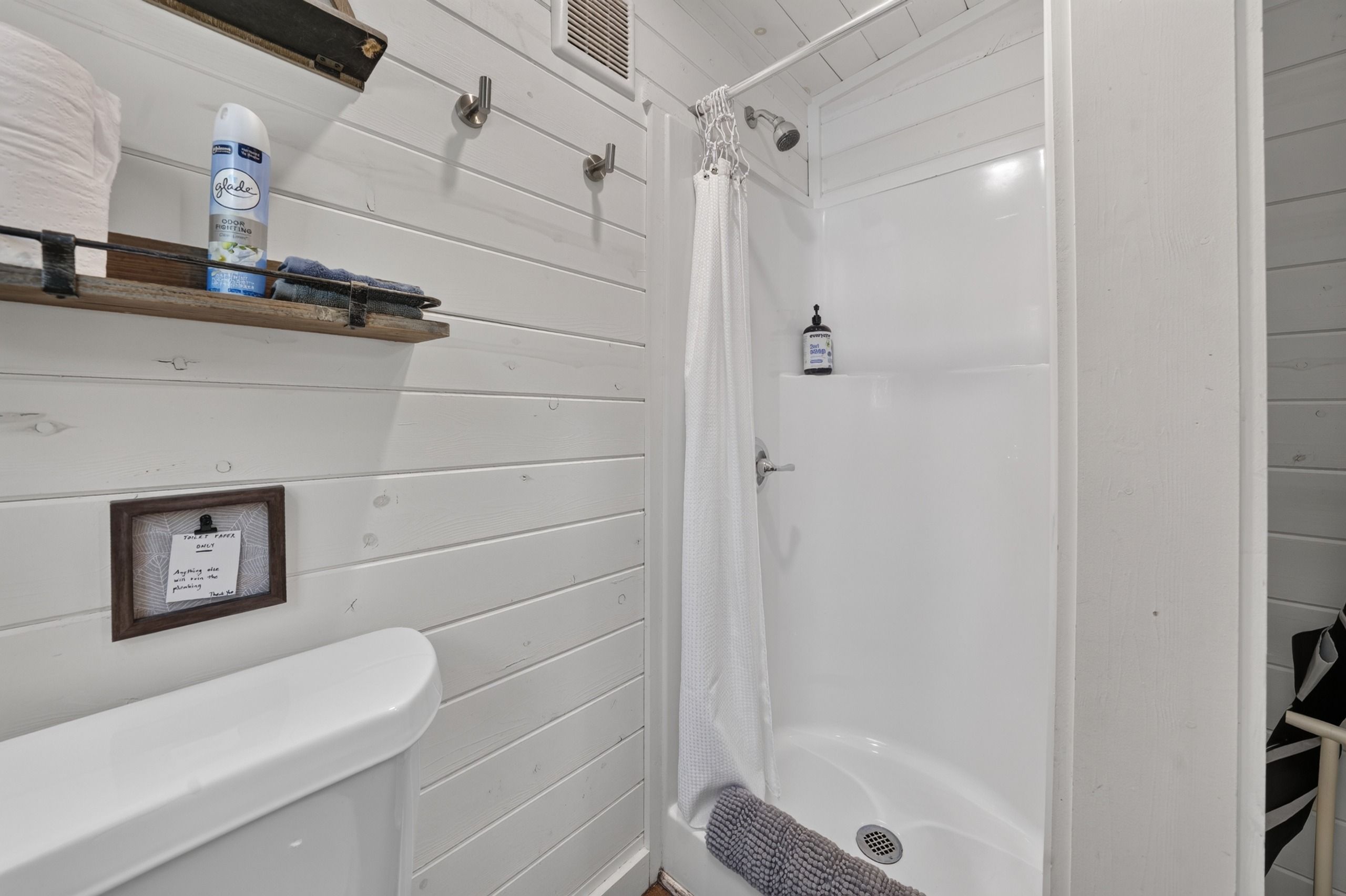 Ein Badezimmer mit Dusche, Toilette und Waschbecken. Ein Handtuchhalter mit Handtuch und einer Flasche Handseife.