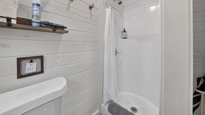 Een badkamer met een douche, toilet en wastafel. Er is een handdoekhouder met een handdoek en een fles handzeep.