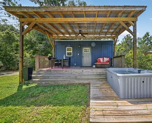 Une terrasse couverte avec un jacuzzi, un coin salon et un petit bâtiment doté d’une porte et de fenêtres.