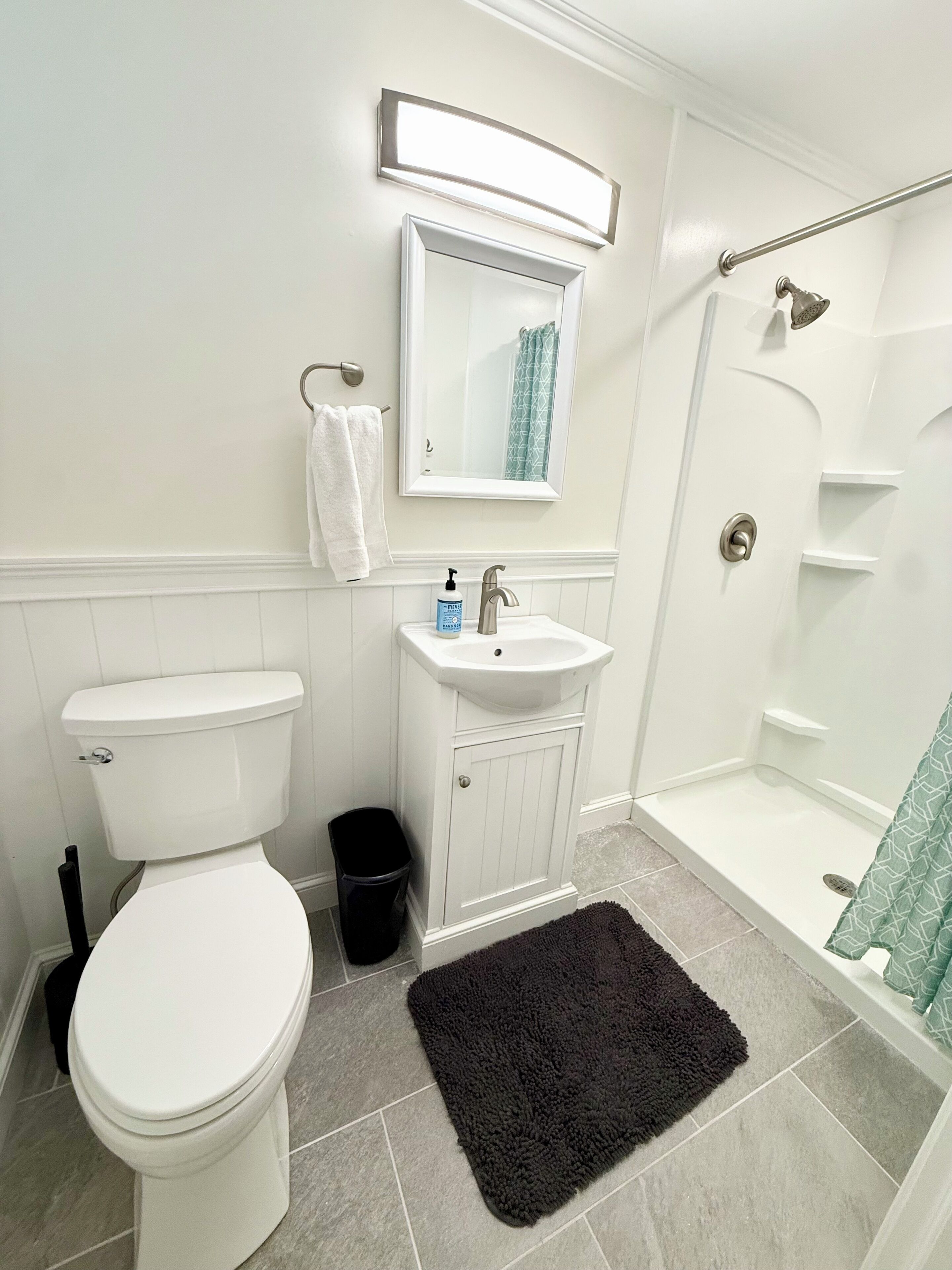 Ein Badezimmer mit Toilette, Waschbecken, Spiegel, Dusche und einem schwarzen Teppich.