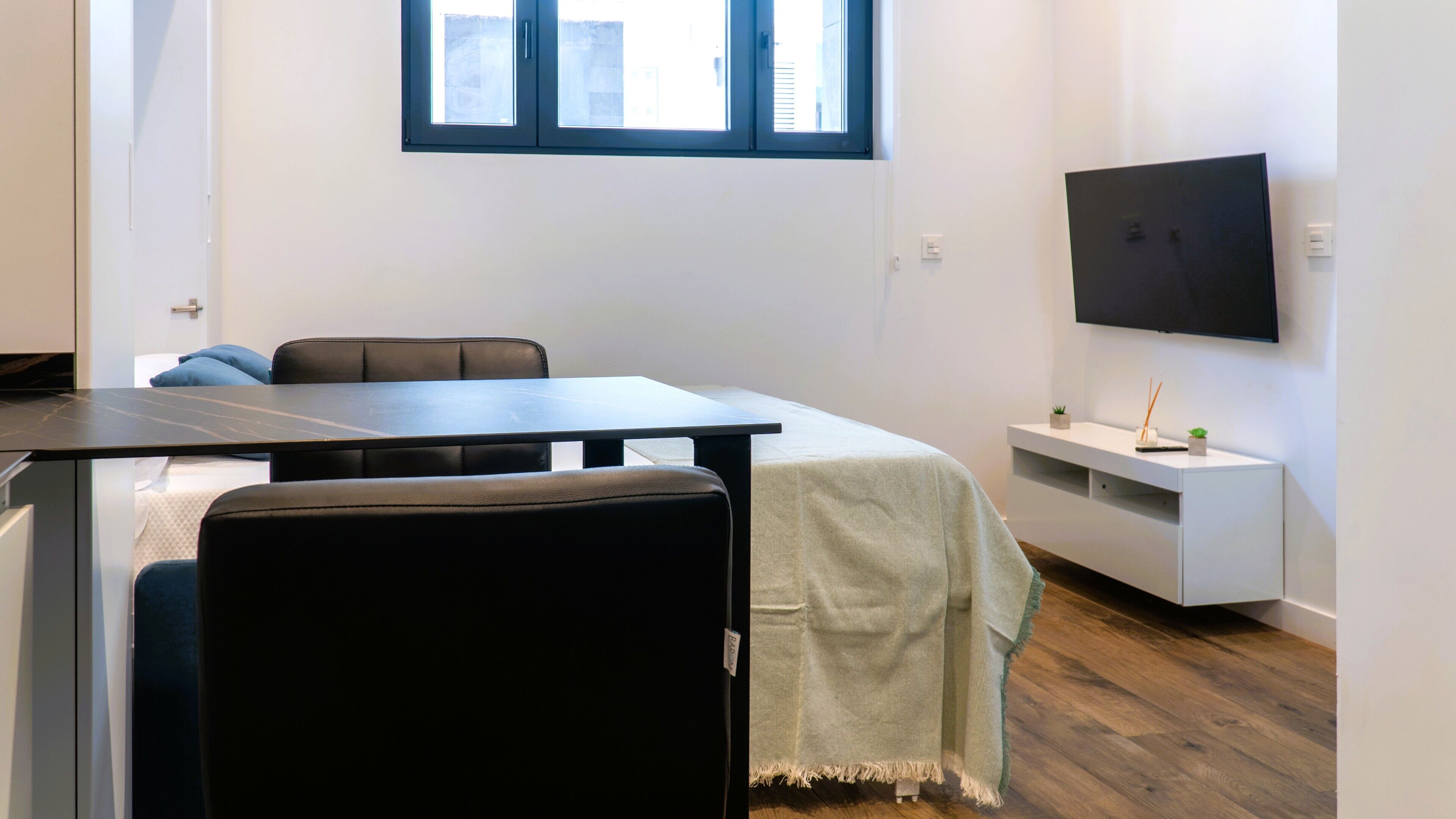 Una habitación moderna con una mesa de comedor, sillas, un televisor montado en la pared y un mueble blanco pequeño.