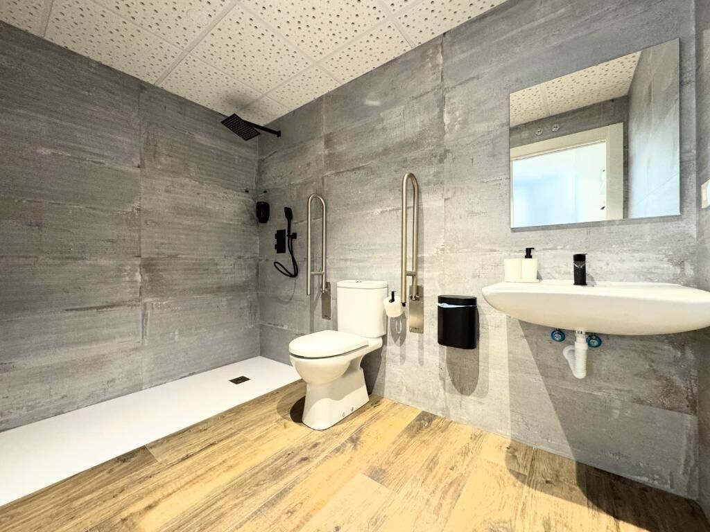 Un baño moderno con pared de concreto, inodoro blanco, lavamanos y zona de ducha.
