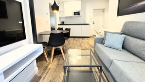 Een moderne woonkamer met een grijze bank, een glazen salontafel en een tv op een witte dressoir.