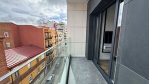 Een hoog gebouw met een glazen balkon met uitzicht op een straat met geparkeerde auto's en omliggende gebouwen.