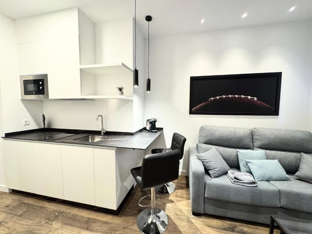 A modern kitchen with a built-in island, a black chair, and a grey sofa in a living area.