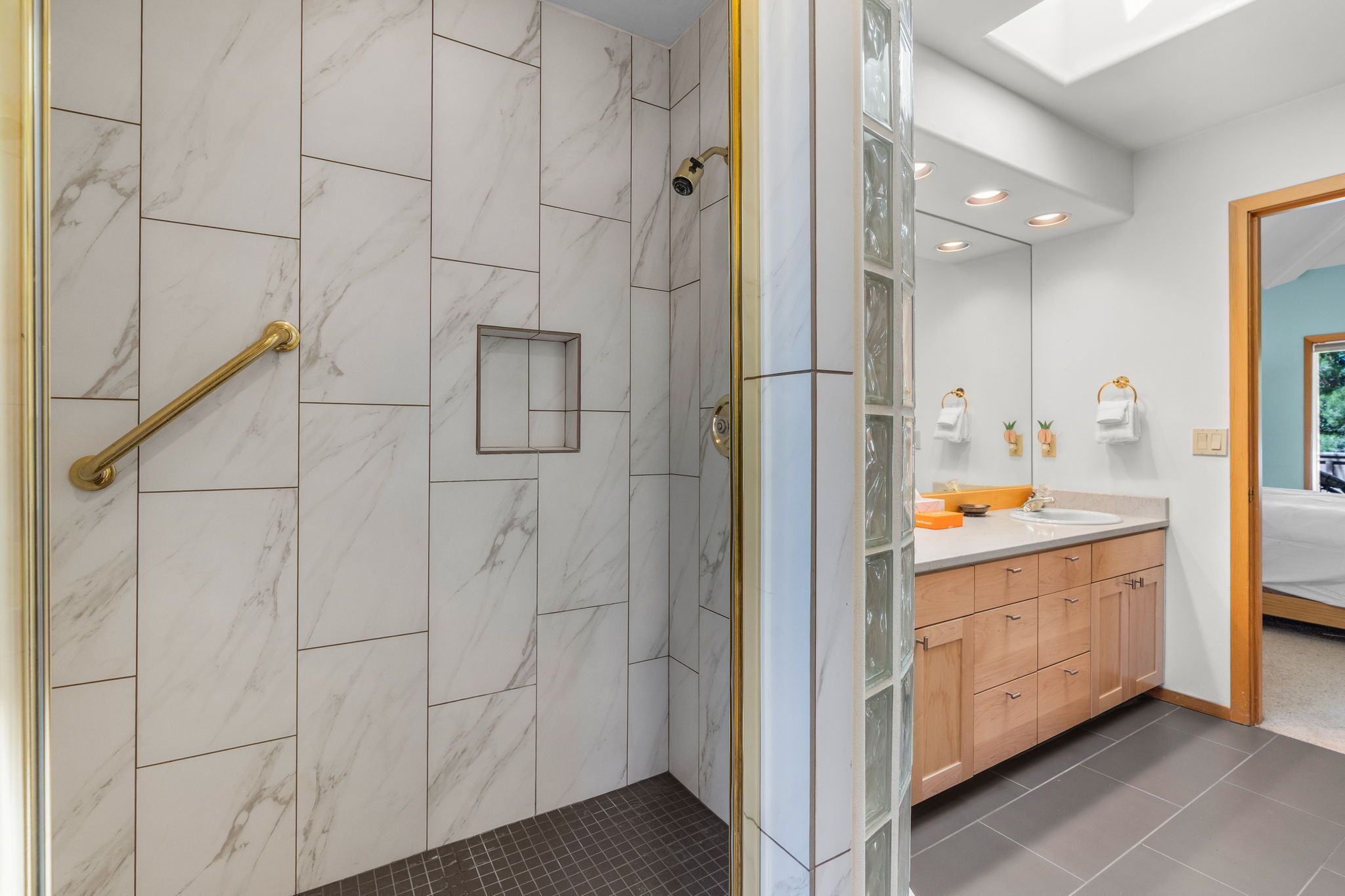 A modern bathroom with a walk-in shower, marble tiles, a glass-enclosed shower area, a wooden vanity with a sink, and a large mirror.