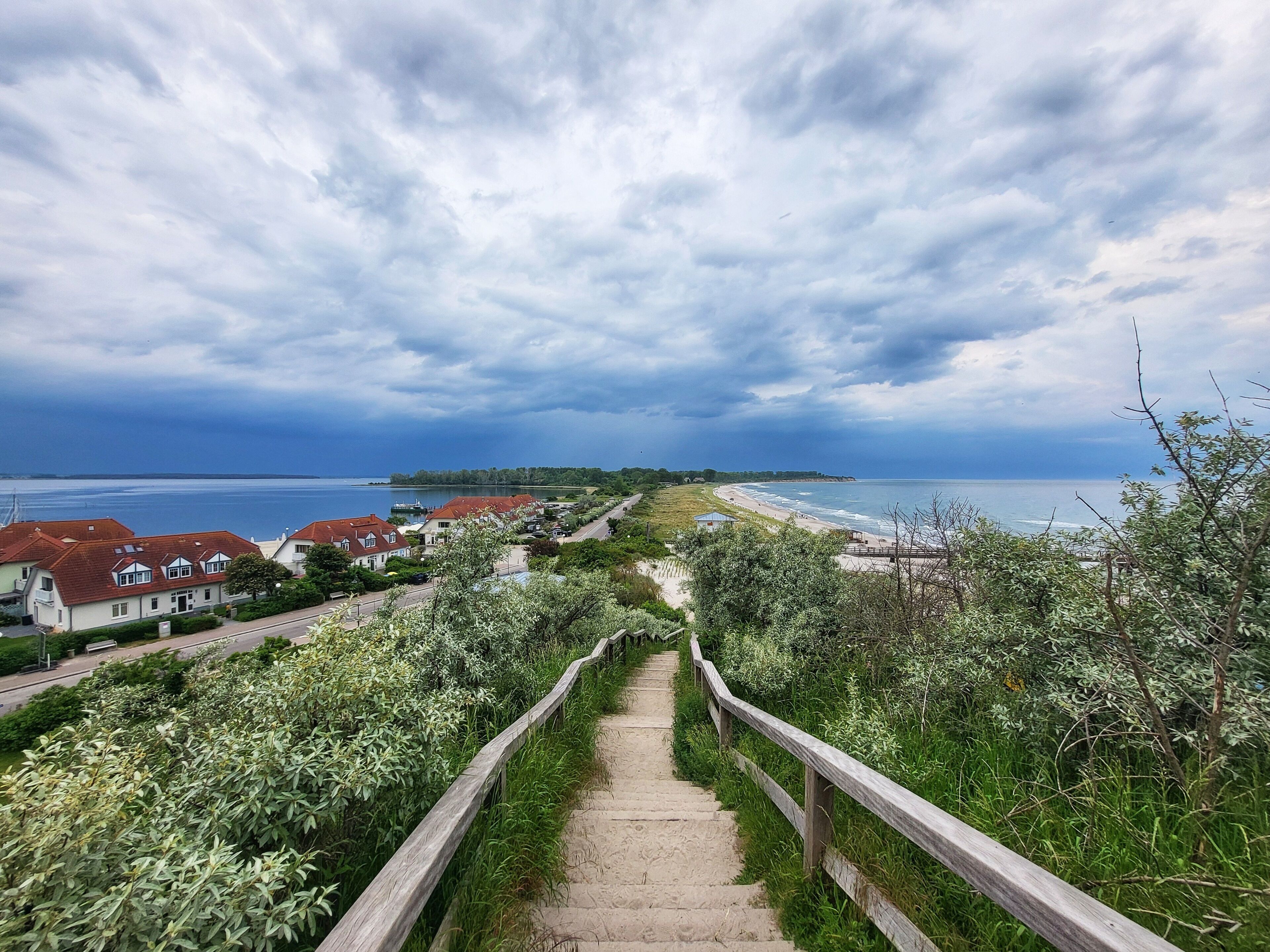 Un sentier côtier qui mène à une plage, avec des maisons en arrière-plan.