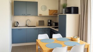Uma cozinha moderna com armários azuis, uma mesa de jantar de madeira com quatro cadeiras brancas e uma janela grande com cortinas.