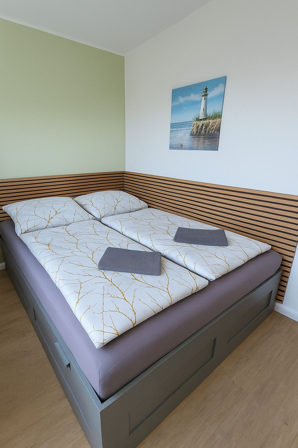 A bed with a patterned mattress, wooden headboard, and a painting of a lighthouse on the wall.