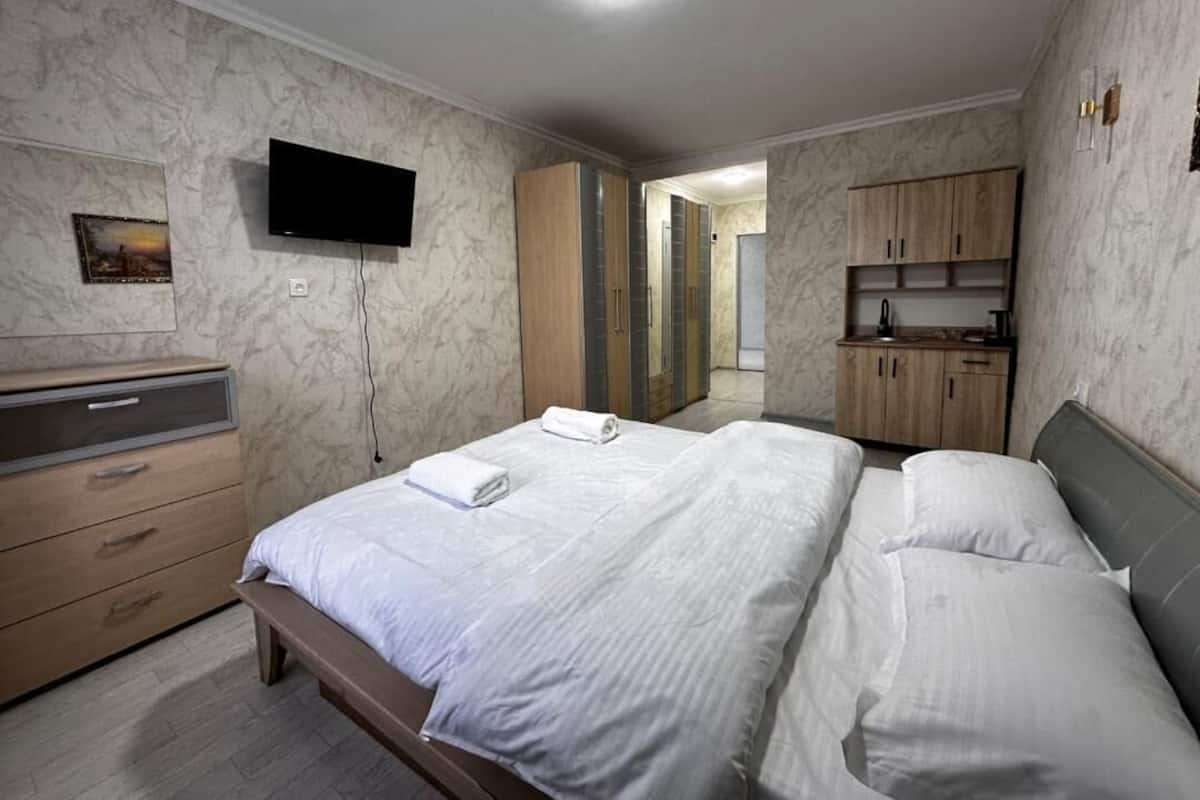 A hotel room with a bed, a TV, a wardrobe, and a bathroom visible in the background.