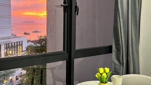 Ein Balkon mit Blick auf einen Sonnenuntergang über dem Meer, ein Tisch mit Stühlen und eine Vase mit Blumen.