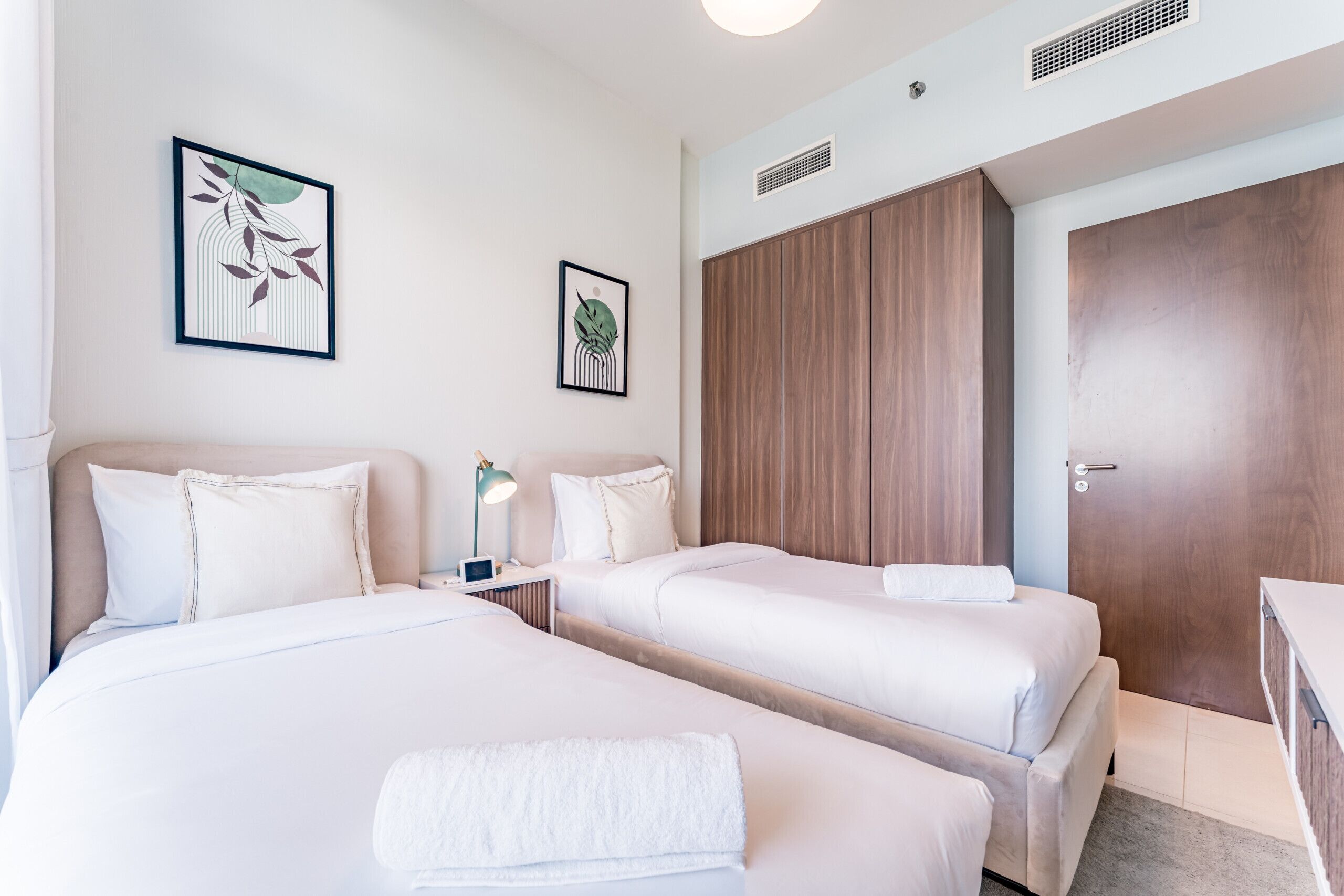 A hotel room with two beds, a wooden wardrobe, and artwork on the walls.