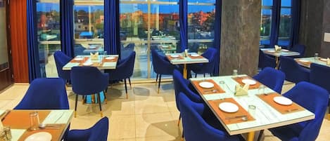 A restaurant with tables and chairs, large windows, and a view of the city.