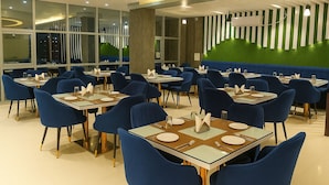 A modern dining area with blue chairs and tables, large windows, and a green wall with vertical stripes. - HOTEL JVW ARENA (Motihari)