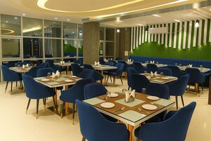 Un comedor moderno con sillas y mesas azules, ventanas amplias y una pared verde con rayas verticales.