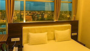 A hotel room with a large bed, a bedside telephone, and a view of the city through large windows. - HOTEL JVW ARENA (Motihari)