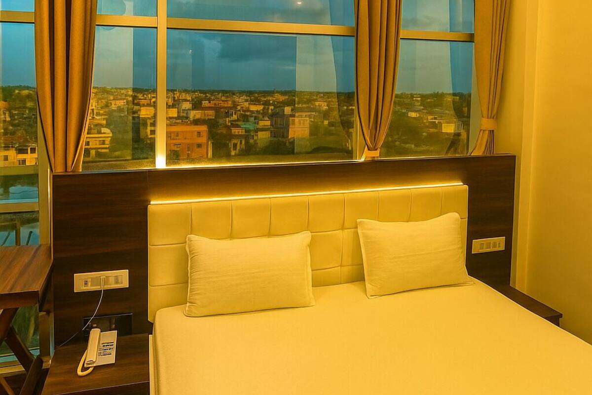 Een hotelkamer met een groot bed, een bedtelefoon en een stadszicht door grote ramen.