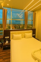 Una habitación de hotel con una cama grande, un teléfono en la mesita de noche y vistas a la ciudad a través de amplios ventanales.