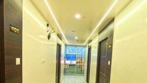 A hotel corridor with a shiny tiled floor, dark wooden doors, and a glass elevator. - HOTEL JVW ARENA (Motihari)
