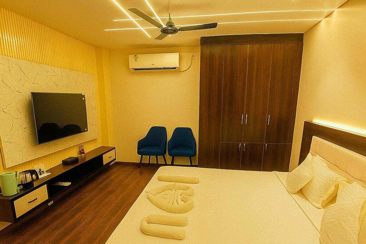 Een moderne hotelkamer met een groot bed, een flatscreen televisie aan de muur, een garderobe en twee fauteuils.