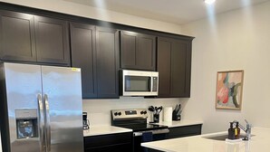 Una cocina moderna con armarios oscuros, electrodomésticos de acero inoxidable, microondas empotrado y piso de madera.