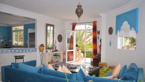 Ein Wohnzimmer mit blauen Sofas, einem Glastisch und einer Küchenzeile mit Herd und Geschirr.