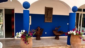 Ein Sitzbereich im Freien mit zwei großen Terrakotta-Pflanzgefäßen mit Blumen, einer Holzskulptur und einer blauen und weißen Wand mit einem gerahmten Bild.