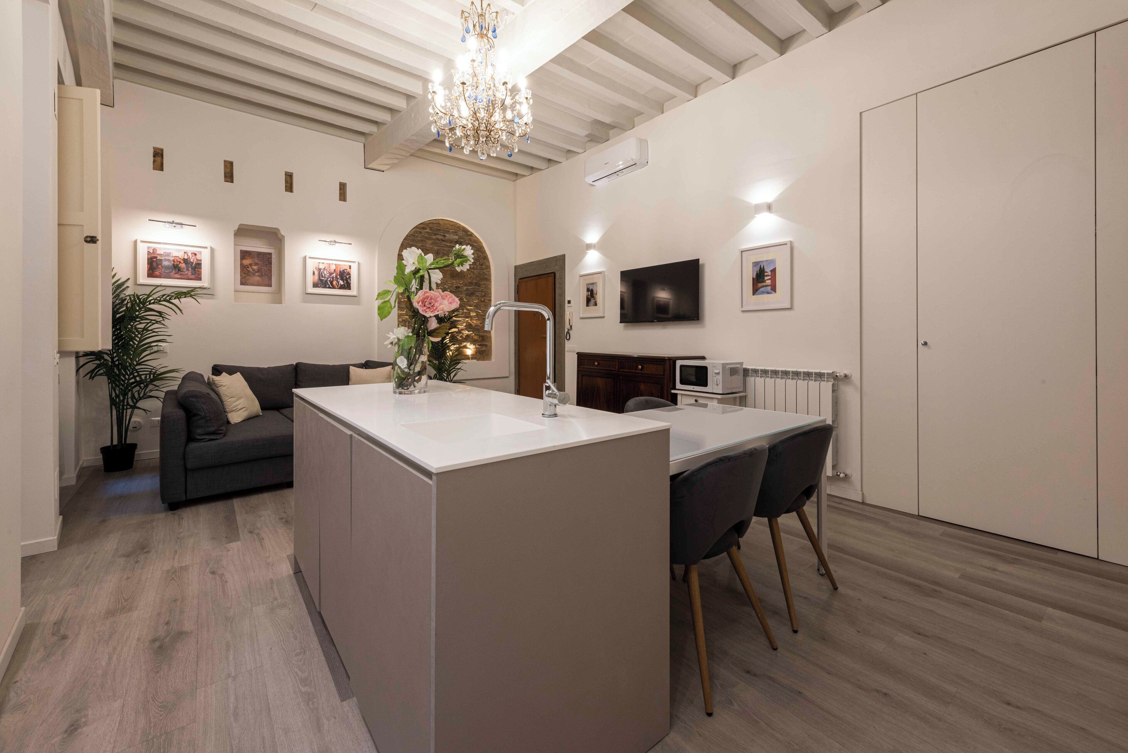 Een moderne keuken met een centraal eiland, een zithoek met stoelen, een bank en een aan de muur bevestigde televisie.