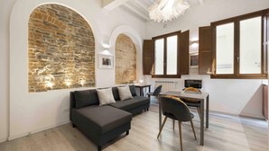 A modern living room with a sectional sofa, a dining table, and a stone accent wall. - Deluxe Pitti Suites by MMega (Florence)