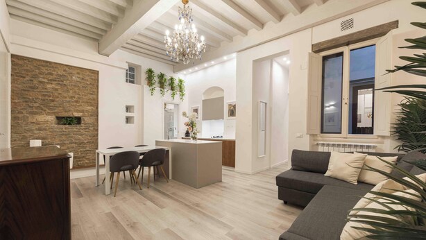 A modern living room with a dining area, a kitchen, and a large window with shutters. - Deluxe Pitti Suites by MMega (Florence)