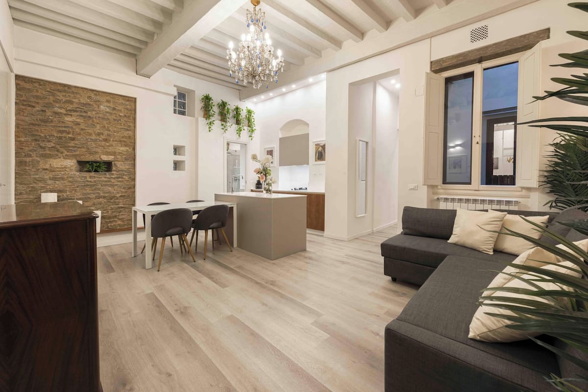 A modern living room with a dining area, a kitchen, and a large window with shutters.