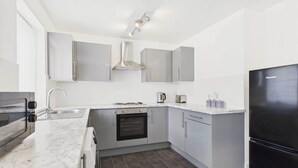 Eine moderne Küche mit grauen Schränken, einem schwarzen Kühlschrank und einem gefliesten Boden.