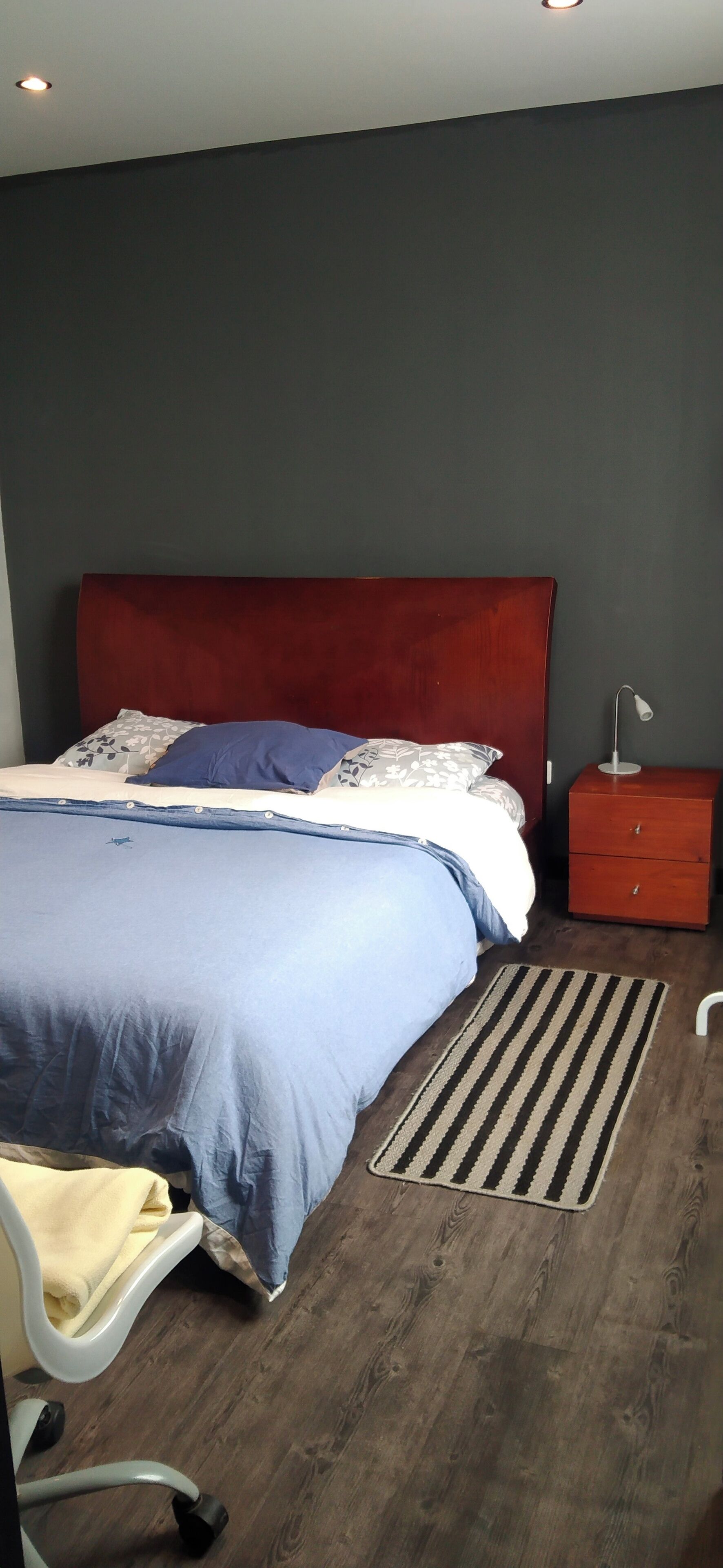 A bedroom with a bed, a nightstand, a desk, and a chair.