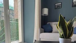 A modern living room with a sofa, a table, a potted plant, and a view of a construction site through a large window. - Terrazza Moio (Naples)