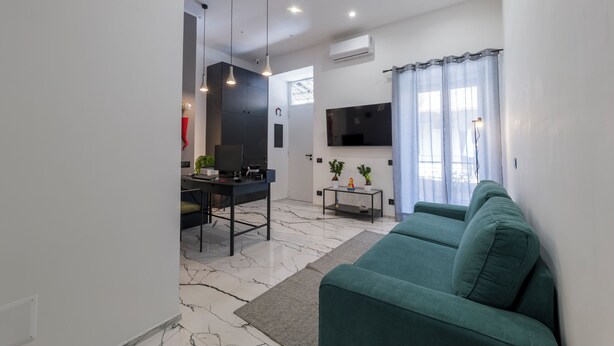 A modern living room with a green sofa, a dining area with a table and chairs, and a kitchen in the background. - Terrazza Moio (Naples)