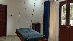 Una habitación con una cama suspendida, una puerta, un armario pequeño y una ventana con cortinas.