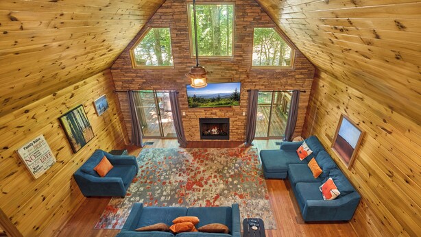 A cozy cabin interior with a fireplace, wooden walls, and a large window overlooking a forest. - Budget-Friendly! Creekside, Hot Tub, Firepit (Gatlinburg)