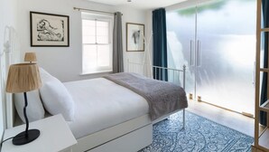 A bedroom with a bed, a bedside table, a lamp, and a large window with curtains. - The Iconic Portobello Mews House (London)
