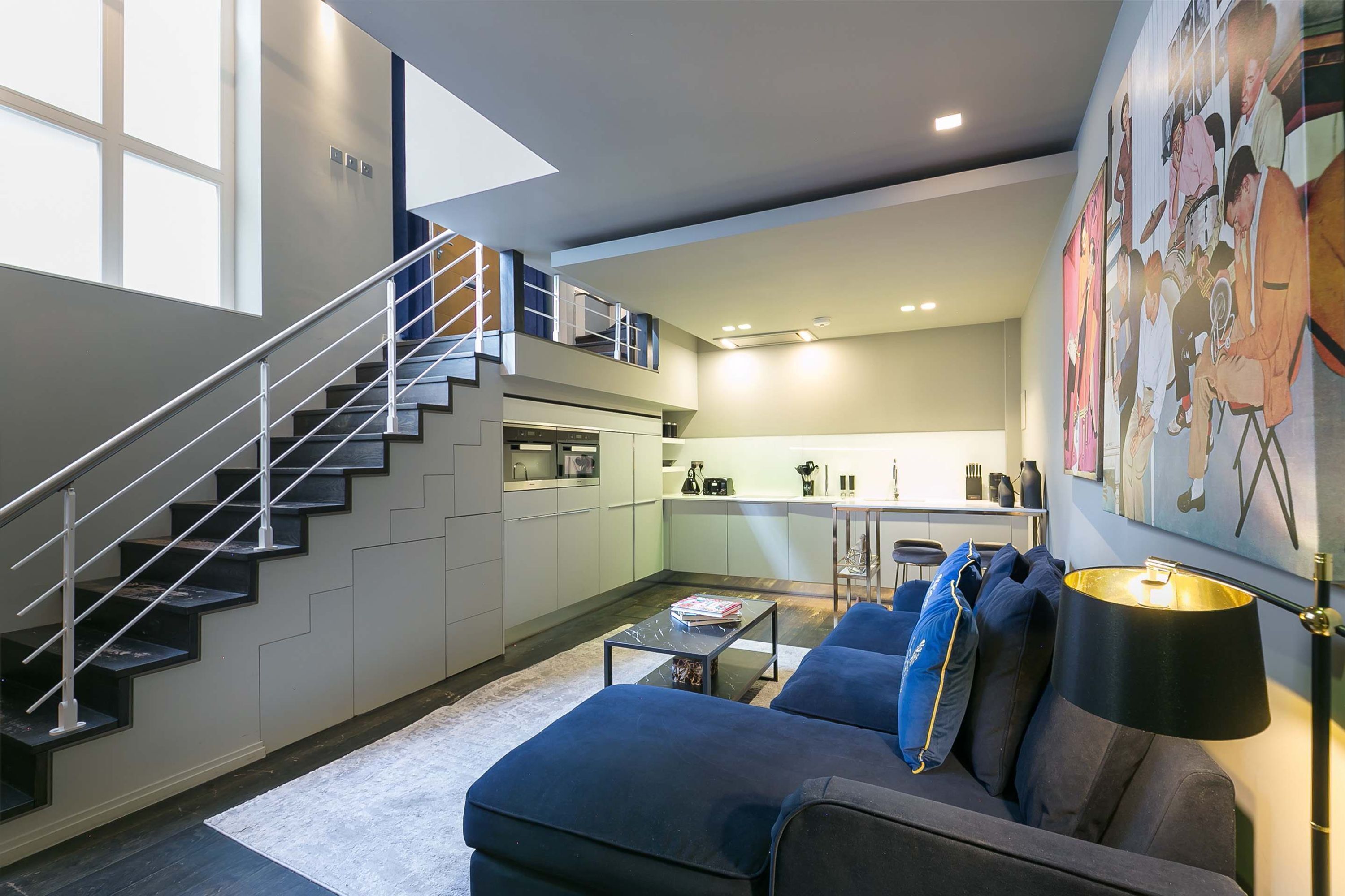 A modern apartment with a staircase, a living area with a sofa and coffee table, a kitchen, and a dining area.