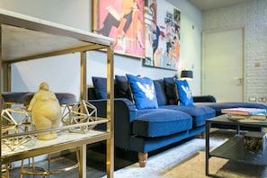 A living room with a blue sofa, a coffee table, and a decorative glass table with a golden frame.