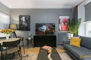 A modern living room with a flat-screen TV, a dining table with chairs, a sofa, a potted plant, and a fireplace. - The Secret Chamber - Covent Garden By Frankie Says (London)